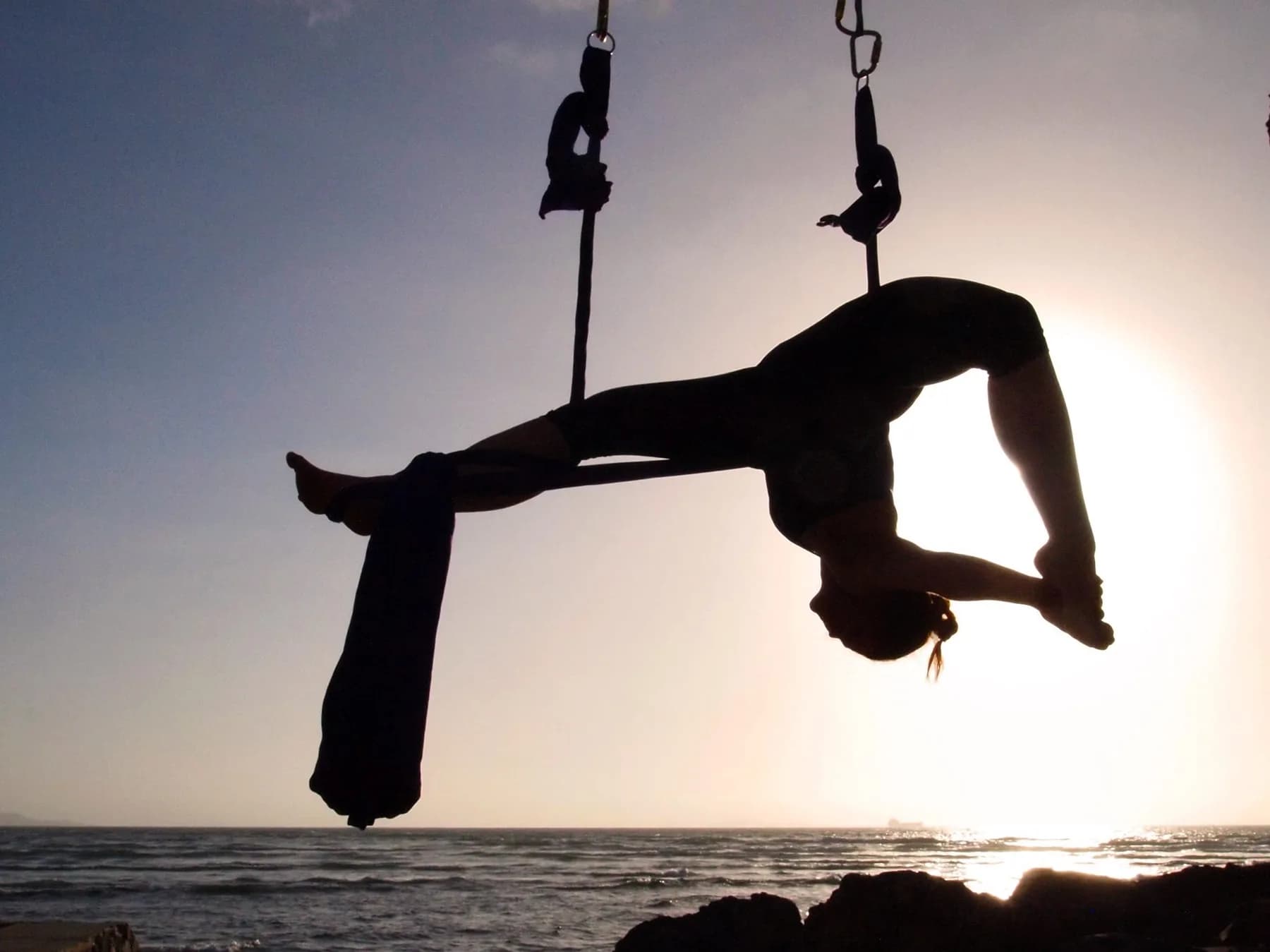 Hannahsita suspended in aerial fabric against a sunset sky