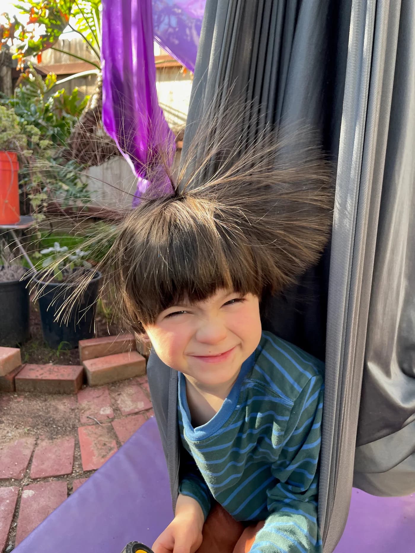 A child smiling while peeking through folds of aerial fabric