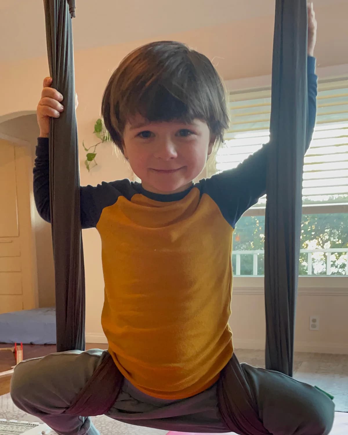 A child smiling while exploring a low aerial fabric above floor mats