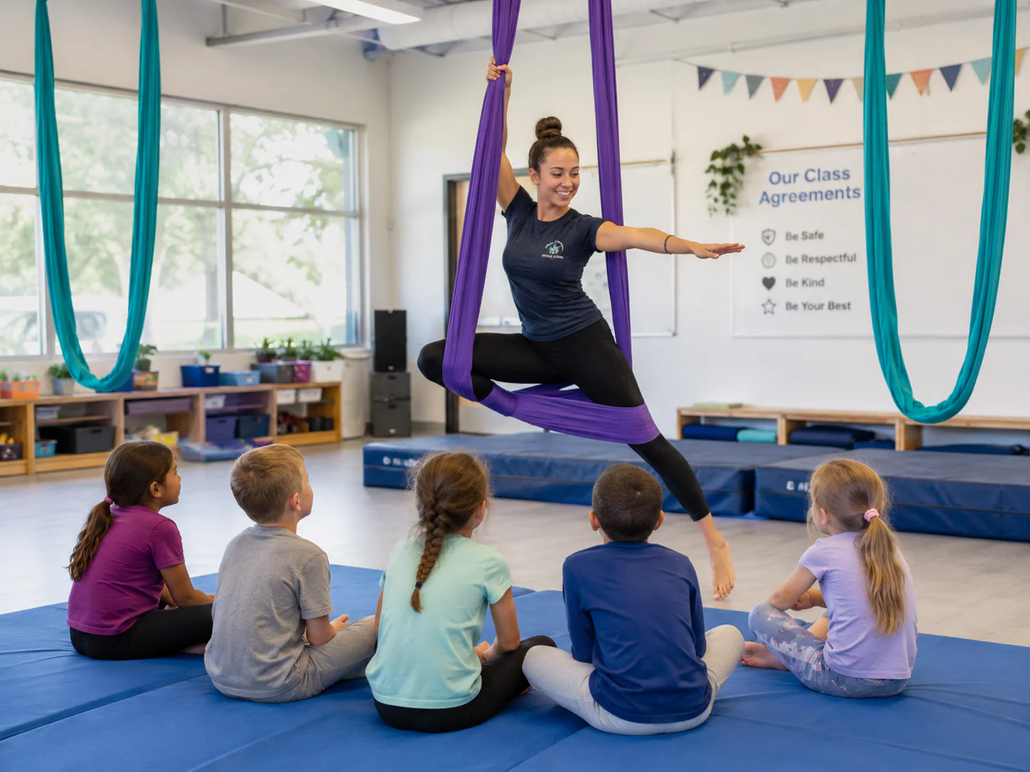 An instructor demonstrating an aerial movement while children watch from floor mats