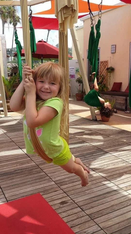 A young child smiling while gently swinging in aerial fabric